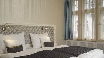 A hotel room with a large bed, a headboard with wall-mounted lights, a window with blue curtains, and a radiator under the window.