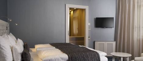A hotel room with a bed, a small table, a chair, a TV, and a door leading to a bathroom.