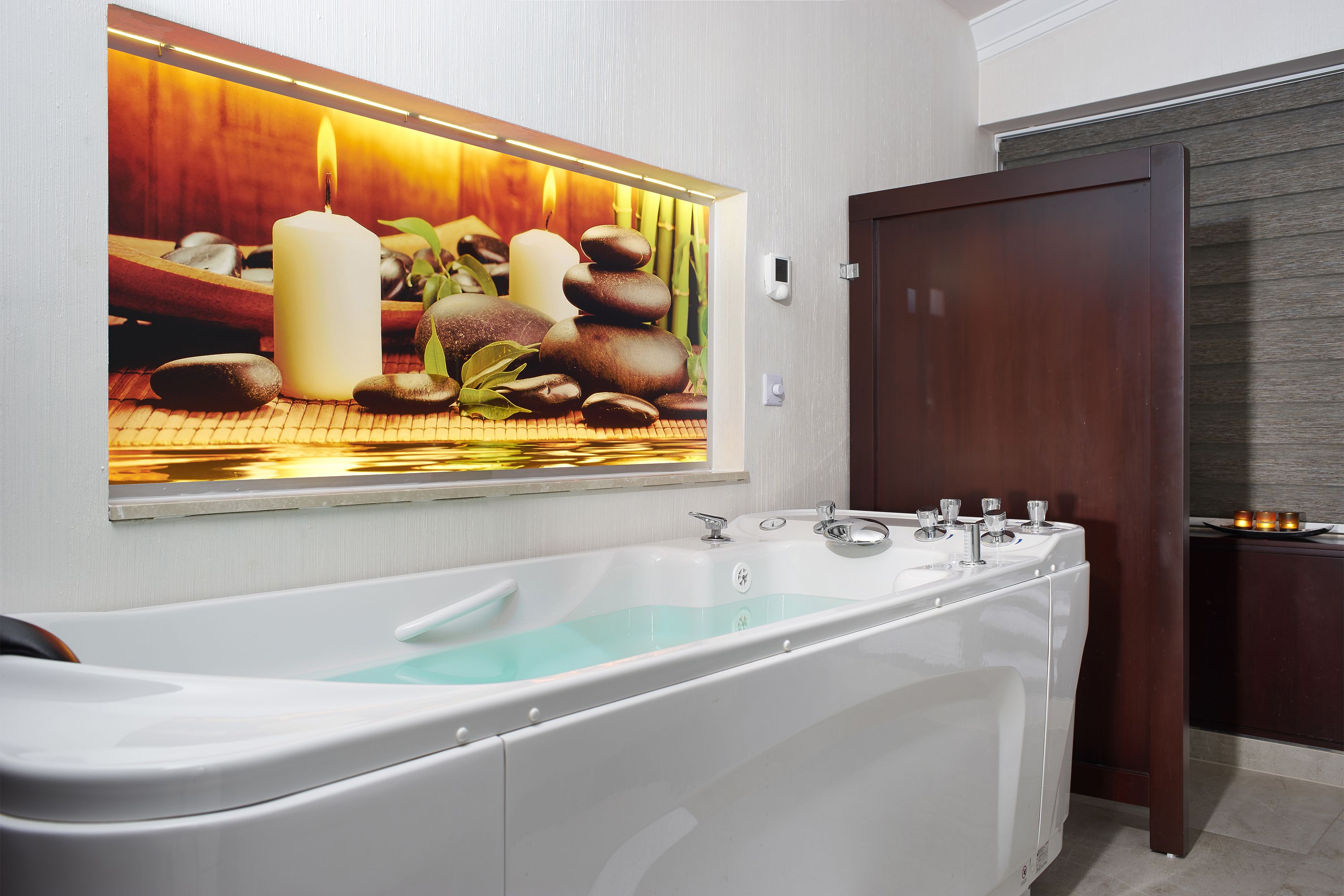 A modern bathroom with a large bathtub, a wall-mounted mirror, and a wooden door.