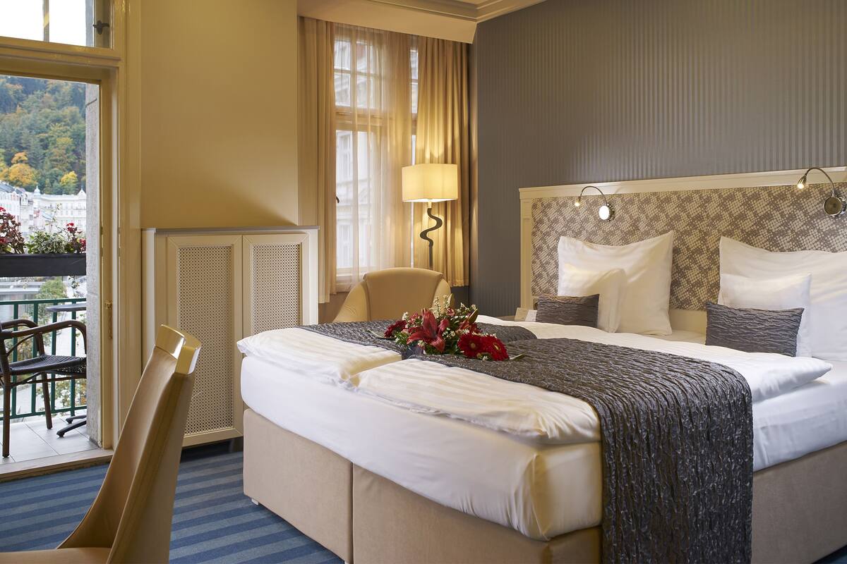 Quarto de hotel com cama grande, uma cadeira, uma mesa e vista para o exterior.