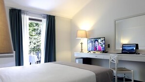 Habitación de hotel con cama, escritorio, computadora, televisor y silla.