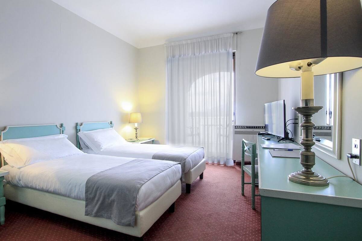 Une chambre d’hôtel avec deux lits, un bureau avec une lampe, une télévision et une fenêtre avec des rideaux.