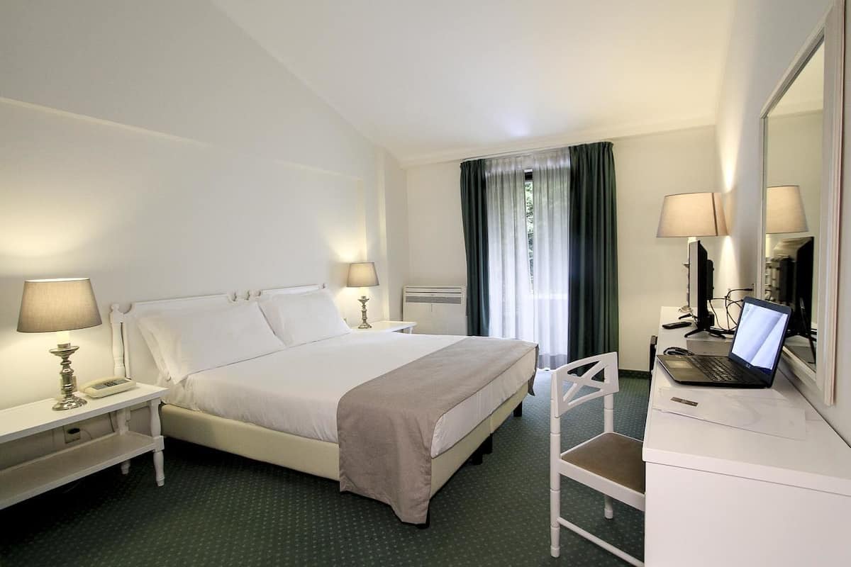 Une chambre d’hôtel avec un lit, des lampes de chevet, un bureau avec un ordinateur portable et un miroir.