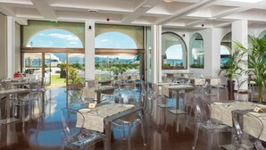 Un restaurante espacioso con sillas y mesas de vidrio transparente, amplias ventanas de arco que ofrecen vistas al exterior y una decoración interior moderna.