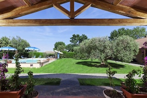 A covered patio with a view of a backyard featuring a swimming pool, lounge chairs, and potted plants. - Fattoria le Spighe (Orbetello)