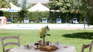 Mesa de refeições ao ar livre posta com pão, um vaso de flores e uma tigela de iogurte.
