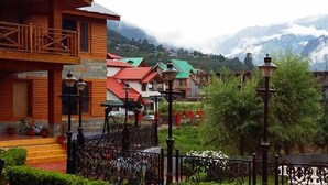 A wooden building with a balcony, surrounded by lush greenery and a mountainous backdrop. - Daffodil Cottages (Manali)