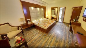 A hotel room with a large bed, a TV, a wooden floor, a desk, and a chair. - Daffodil Cottages (Manali)