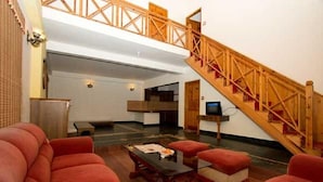 A spacious living area with a high ceiling, a wooden staircase, and a modern kitchen in the background. - Daffodil Cottages (Manali)