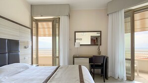 A hotel room with a bed, a desk, a mirror, and a view of the beach. - Hotel Capri & Residence (Camaiore)