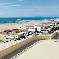 A coastal town with a beach, a pier, and buildings with red roofs.