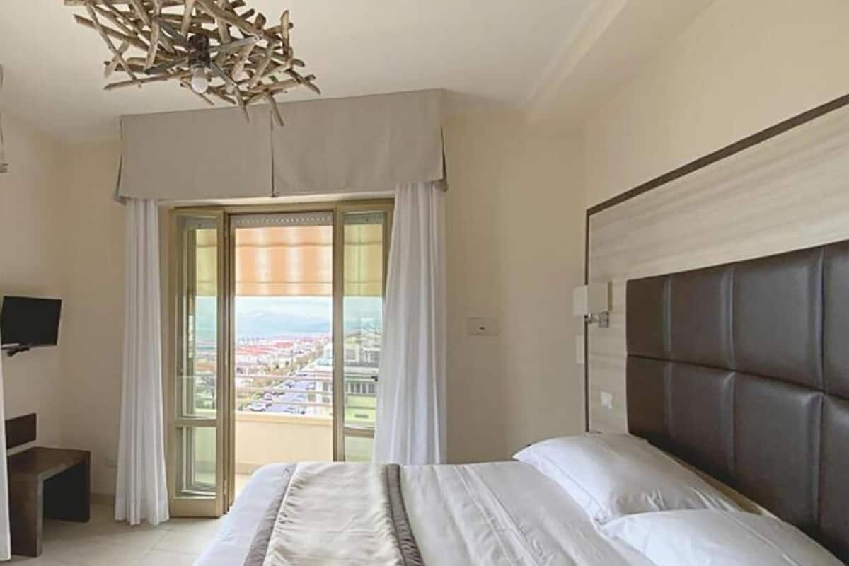 A hotel room with a bed, a television, a desk, and a view of a cityscape through the window.