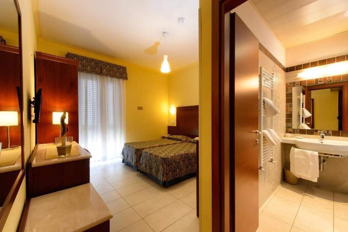 A hotel room with a bed, bedside table, lamp, and a bathroom with a sink and mirror.
