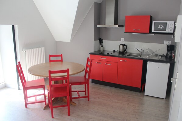 Une cuisine compacte aux couleurs rouge et blanche, comprenant une table de salle à manger ronde avec quatre chaises, un four à micro-ondes, une bouilloire et un évier.