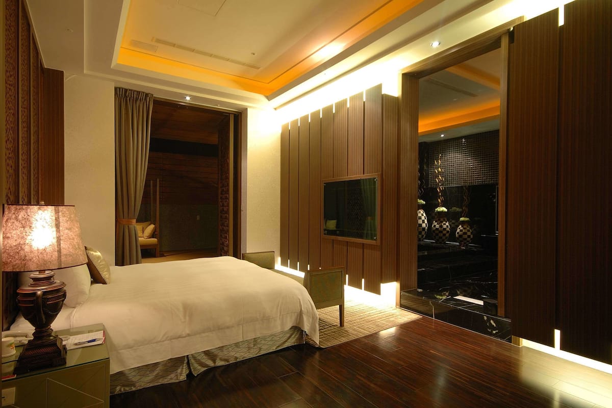 A hotel room with a large bed, a TV mounted on the wall, and a wooden floor.