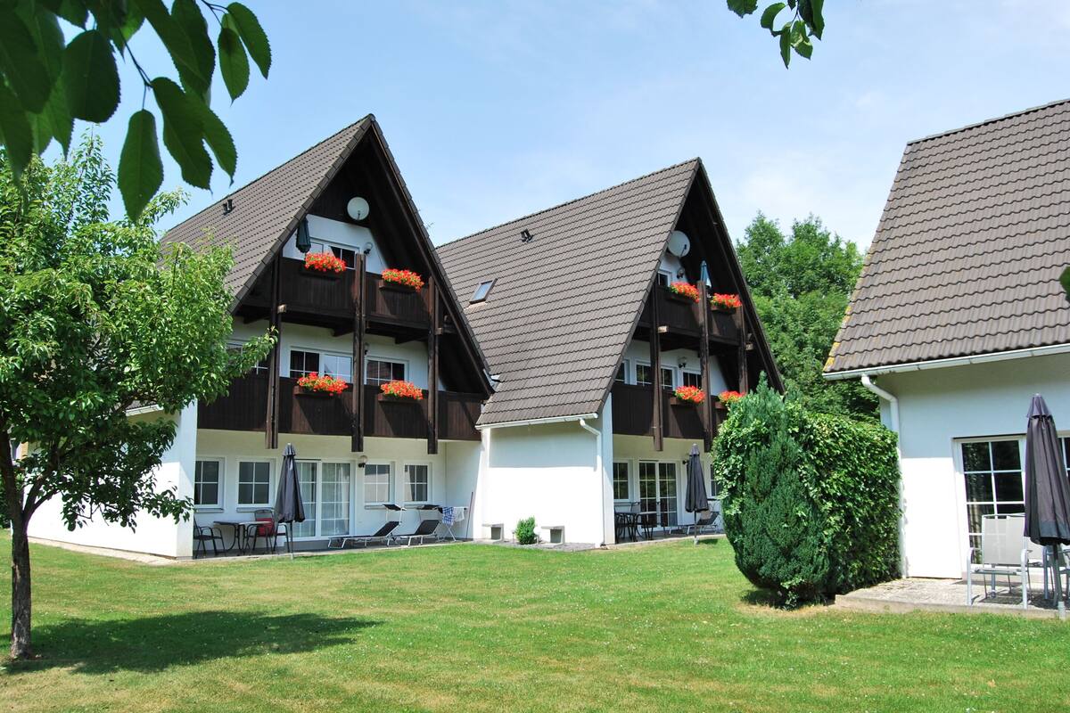 Un bâtiment à deux étages, doté d’un toit en pente, de balcons ornés de jardinières et d’une pelouse bien entretenue.