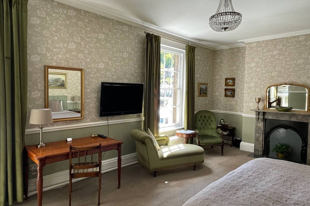 A hotel room with a bed, a desk, a chair, a television, a fireplace, and a window with curtains.