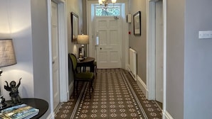 A hallway with patterned flooring, a chandelier, and framed pictures on the walls. - Ashdale Guest House (Matlock)