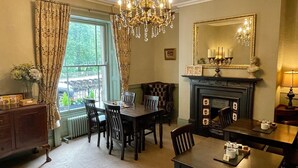A dining area with a fireplace, a chandelier, and a view through the window. - Ashdale Guest House (Matlock)