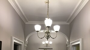 A hallway with a patterned floor, a chandelier, and a door with a clock. - Ashdale Guest House (Matlock)