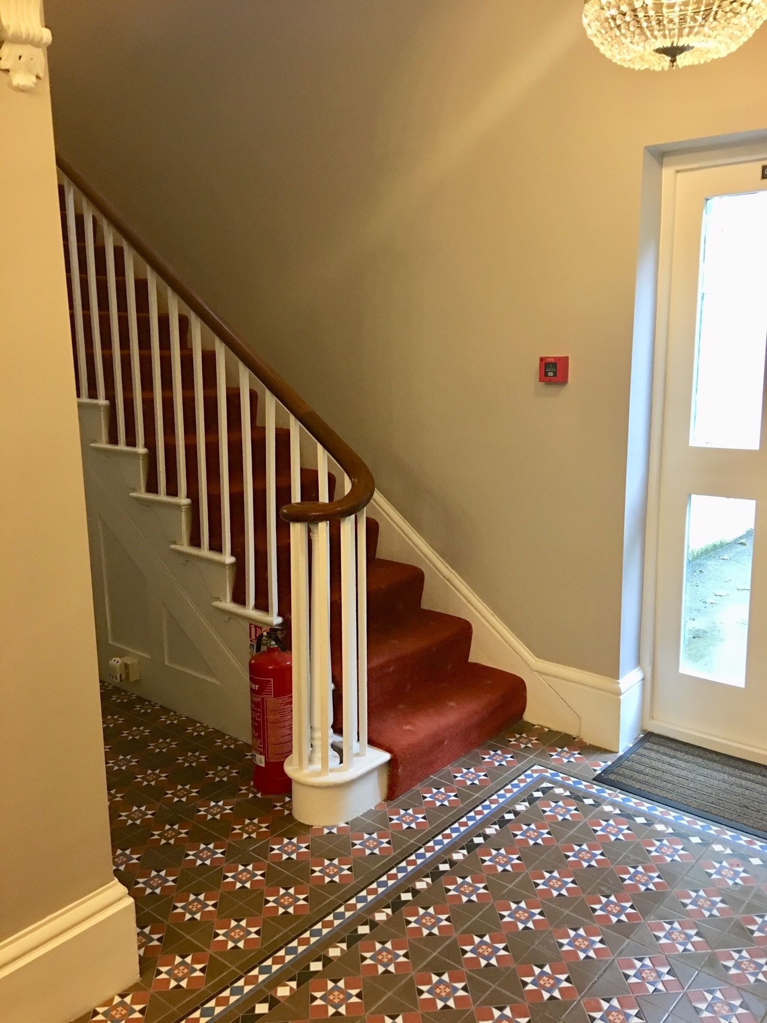 A staircase with white balusters and red carpeted steps leading to a door with a glass panel.