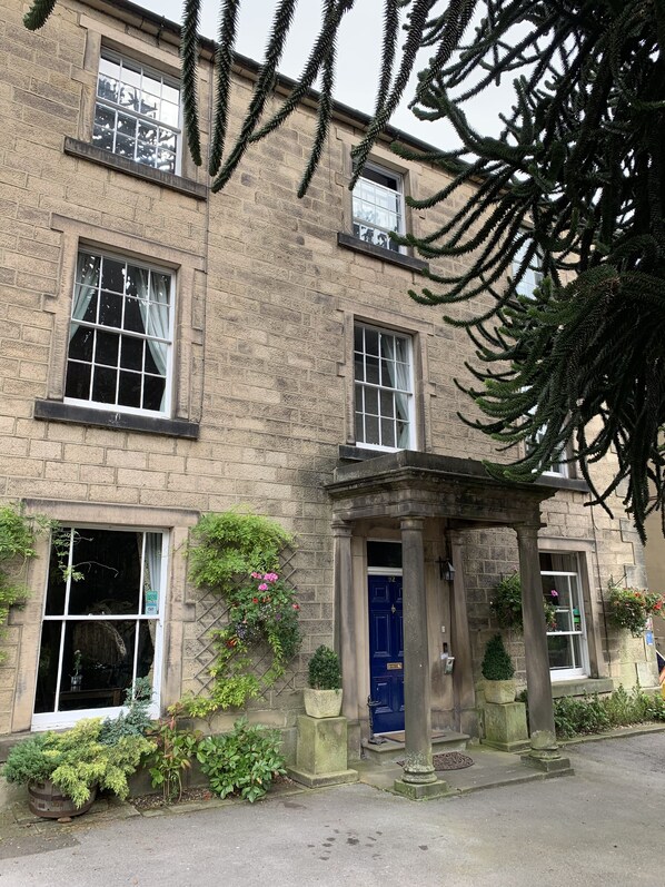 A stone building with multiple windows, a blue door, and a small porch with columns. - Ashdale Guest House (Matlock)