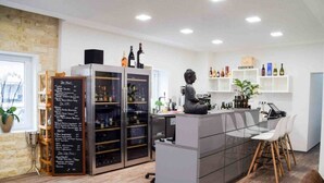 Zona de bar moderna con mostrador de cristal, sillas de madera y una estatua. Se observan estantes con botellas y un menú en una pizarra.