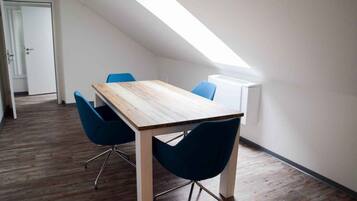 Una habitación moderna con una mesa de madera y sillas azules, techo inclinado y una puerta al fondo.
