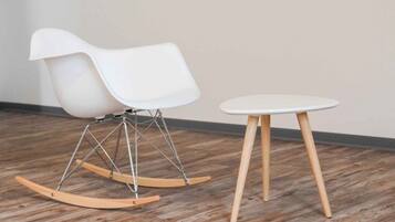 Une chaise à bascule blanche et une petite table ronde aux pieds en bois.