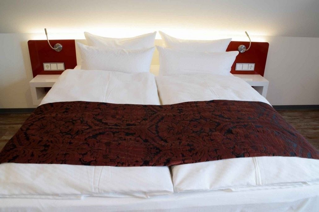 A neatly made bed with a red and white patterned bedspread, white pillows, and a red headboard.
