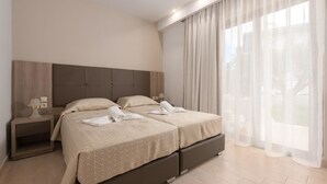 A modern hotel room with a large bed, a nightstand, and a window with sheer curtains. - Saint George Resort (Rhodes)
