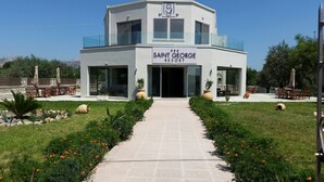 A modern building labeled "SAINT GEORGE RESORT" with a central entrance, outdoor seating, and a well-maintained garden. - Saint George Resort (Rhodes)