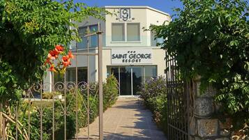 The entrance to Saint George's Resort with a clear pathway leading to the main entrance, surrounded by lush greenery and a metal gate.