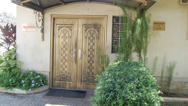 Une porte en bois à deux battants ornée de motifs complexes, une enseigne indiquant un restaurant et un bar, et une entrée couverte avec un toit en métal.