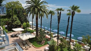 Un complejo turístico frente al mar con terraza al aire libre, palmeras y vistas al océano.