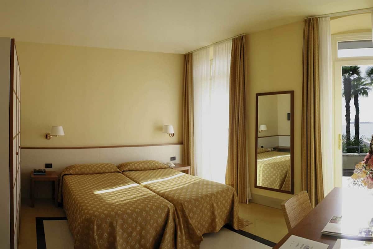 A hotel room with two beds, a desk, a chair, a mirror, and a window with curtains.