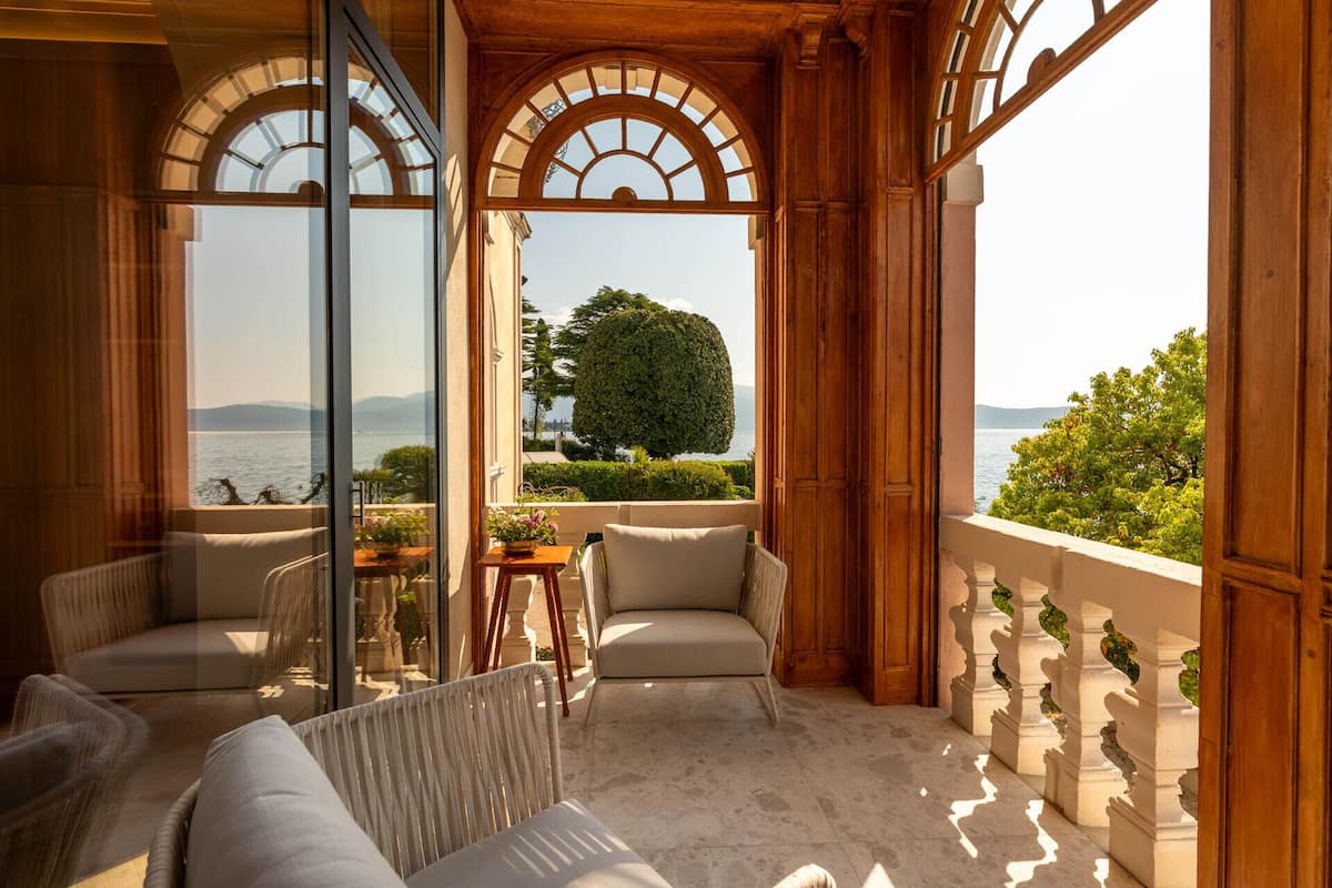 A balcony with a view of the sea, furnished with a sofa and chairs, and a table with a potted plant.
