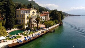 Un hotel grande con piscina, situado junto a un lago y montañas al fondo.