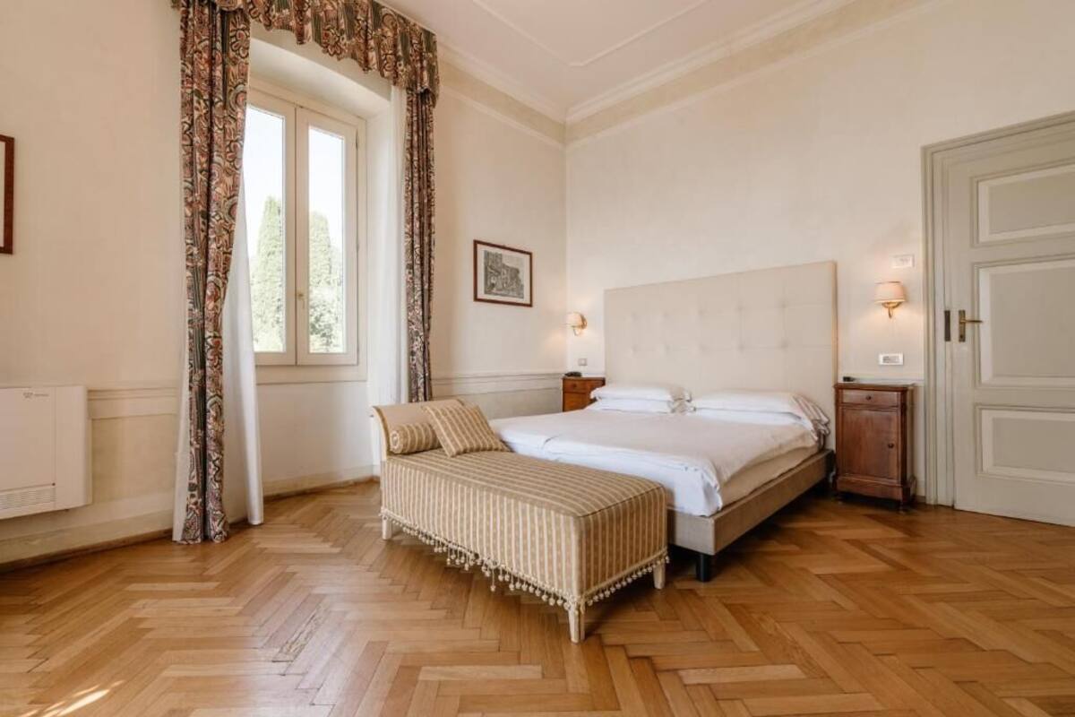 A bedroom with a large bed, a bedside table, a nightstand, a window with curtains, and a door.