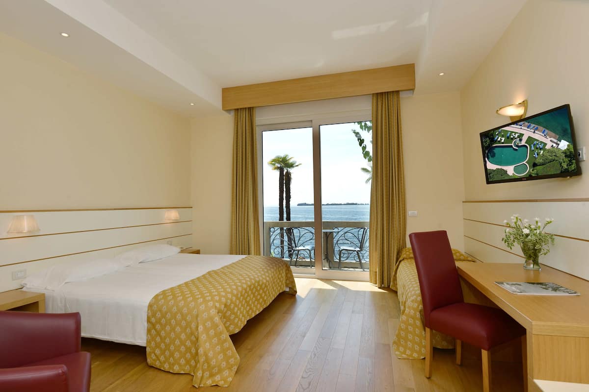 A hotel room with a bed, a desk, a chair, a TV, and a balcony with a view of the sea.