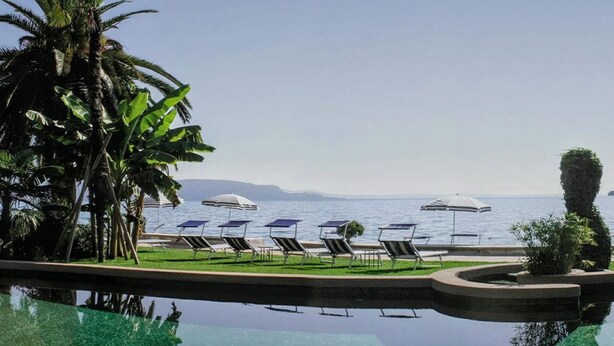 Zona de piscina con sillones de playa y sombrillas, vista despejada al mar, y entorno tropical con palmeras.