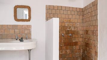 Un baño con lavamanos blanco, un espejo y una zona de ducha con pared de ladrillo.