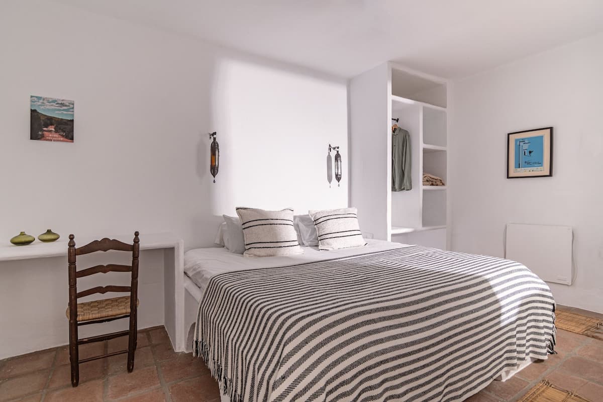 A bedroom with a bed, a wooden chair, a white shelf, and a white wardrobe.