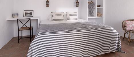A bedroom with a bed, a chair, a shelf with storage boxes, and two wall-mounted lanterns.