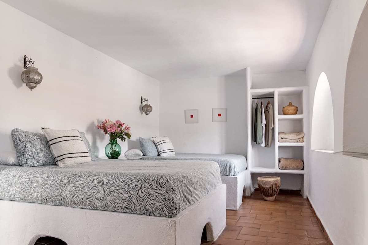 A bedroom with two beds, a small seating area, and a storage unit.