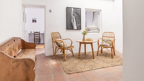 Un espacio de sala acogedor con un sofá de madera, dos sillones de mimbre, una mesita redonda con un florero y obras de arte en las paredes.