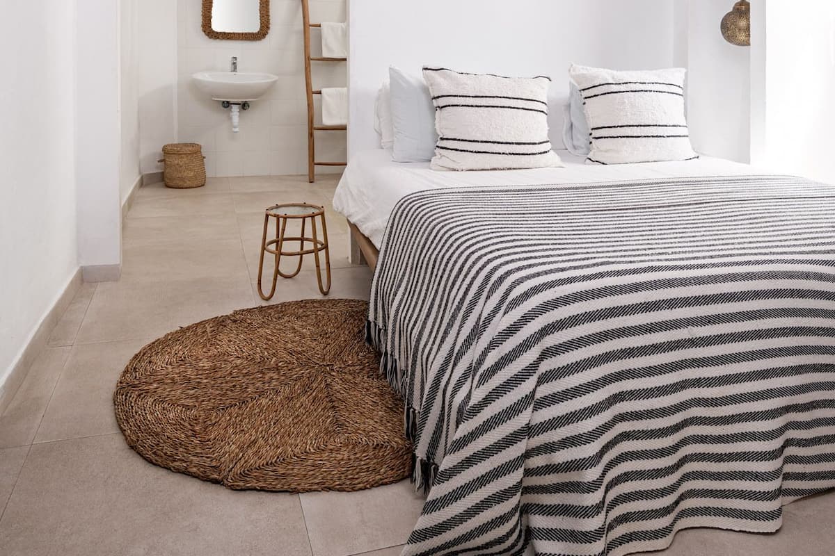 A minimalist bedroom with a bed, a round woven rug, and a hanging light fixture.