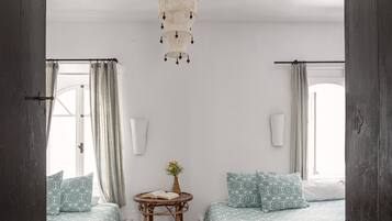 A room with two beds, a small table with a book and flowers, and a hanging light fixture.