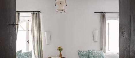 A room with two beds, a small table with a book and flowers, and a hanging light fixture.