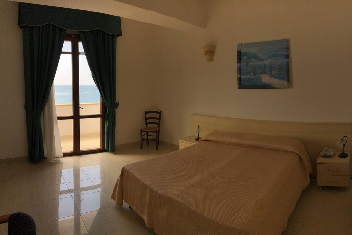 A bedroom with a bed, a chair, a nightstand, and a painting on the wall.